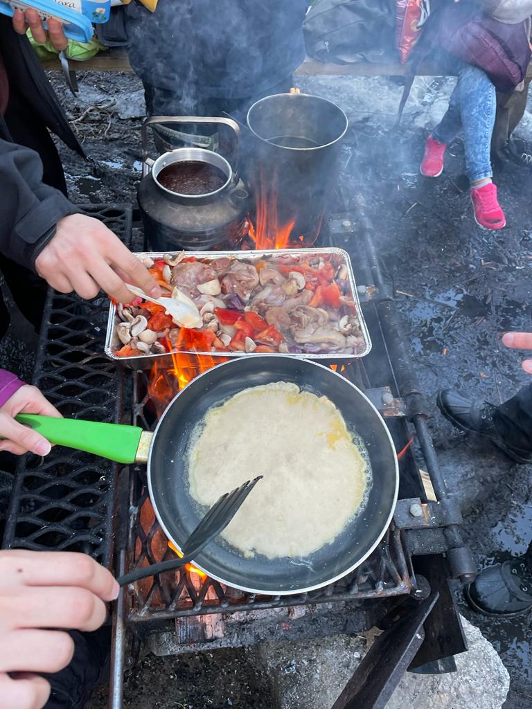 Hands preparing pancakes and a shared meal over a campfire